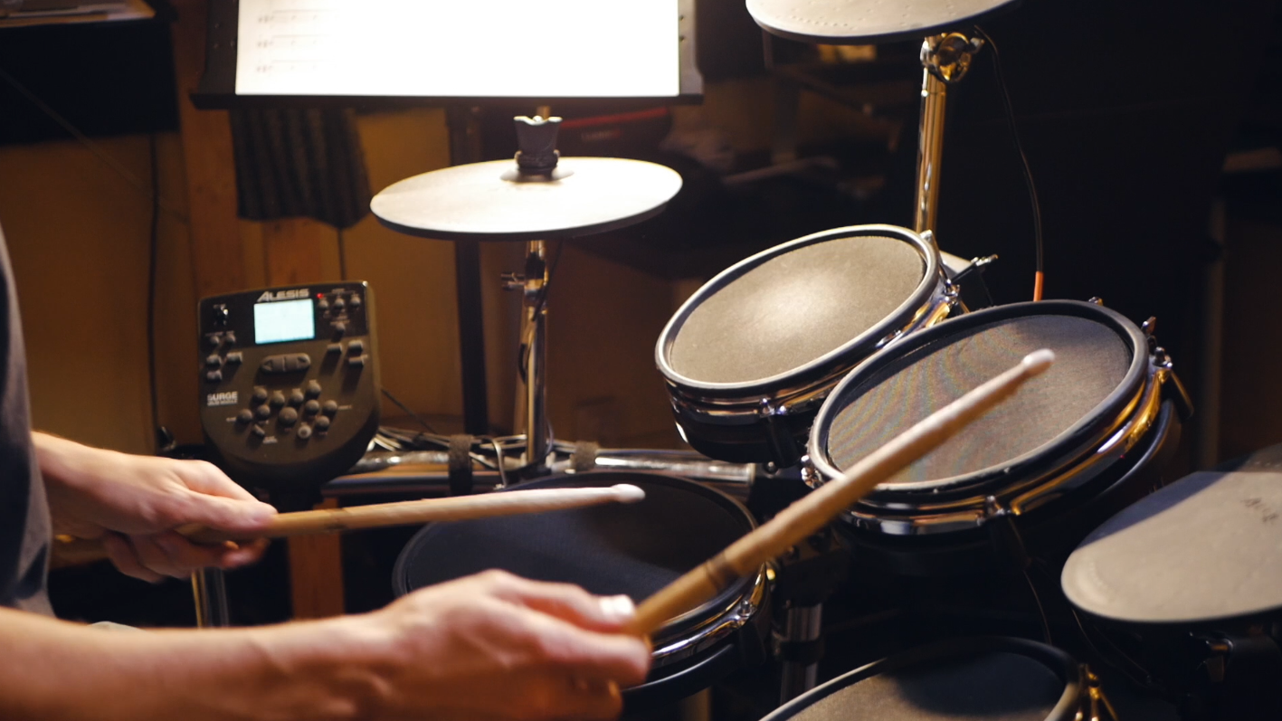 Baterista tocando una batería electrónica con auriculares en casa